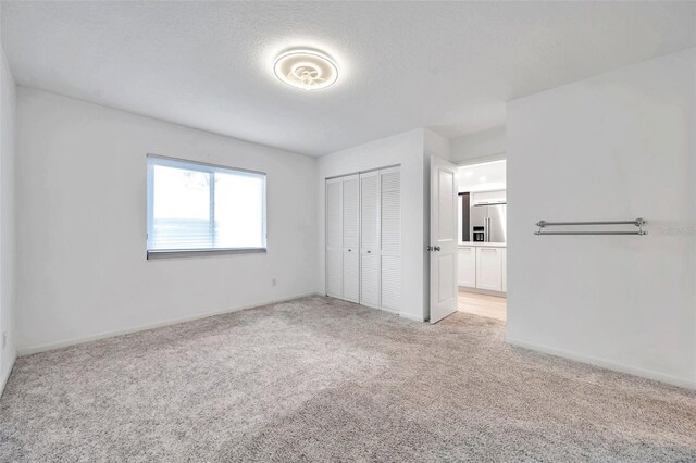 unfurnished bedroom featuring light colored carpet, baseboards, a textured ceiling, a closet, and high end fridge