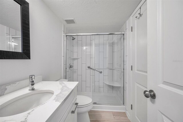 full bathroom featuring toilet, visible vents, a shower stall, a textured ceiling, and vanity