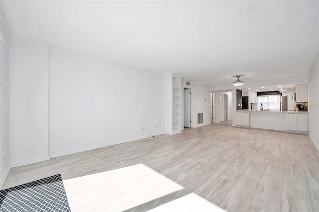 unfurnished living room featuring baseboards, light wood-type flooring, built in features, visible vents, and a sink