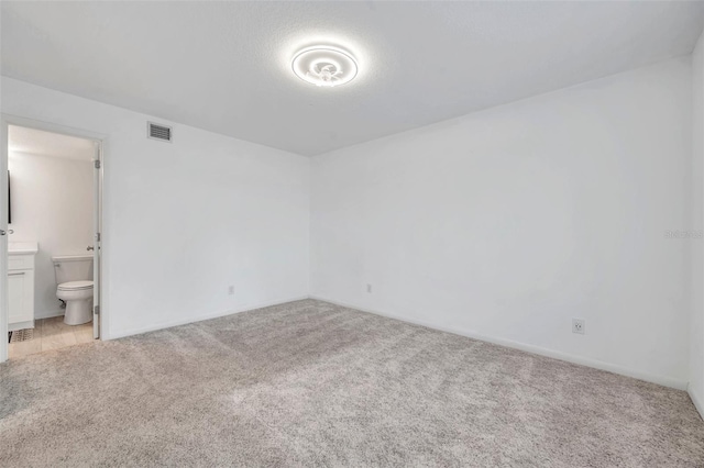 unfurnished bedroom with light carpet, baseboards, ensuite bathroom, and visible vents