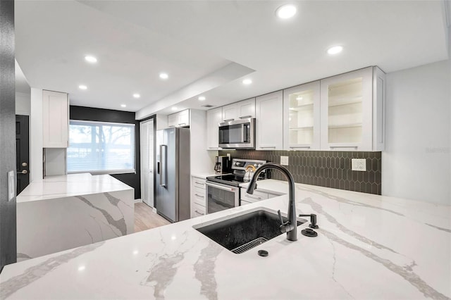 kitchen featuring glass insert cabinets, white cabinets, stainless steel appliances, and light stone counters