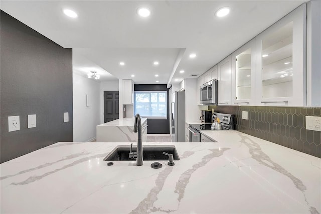 kitchen with stainless steel appliances, white cabinetry, light stone countertops, a sink, and glass insert cabinets