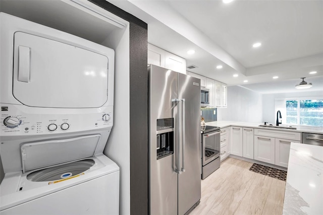 clothes washing area featuring stacked washer / dryer, a sink, light wood-style flooring, recessed lighting, and laundry area