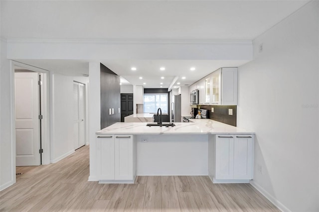 kitchen featuring a peninsula, white cabinetry, appliances with stainless steel finishes, a sink, and light wood-style floors