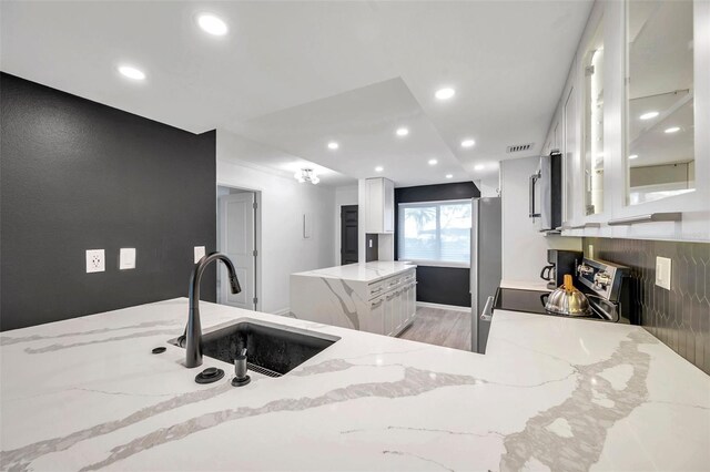 kitchen with glass insert cabinets, white cabinetry, stainless steel appliances, a sink, and light stone counters