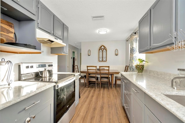 kitchen with light stone counters, gray cabinetry, a textured ceiling, electric stove, and light hardwood / wood-style floors