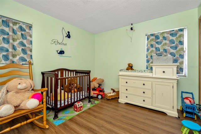 bedroom with dark wood-type flooring, a nursery area, and a textured ceiling