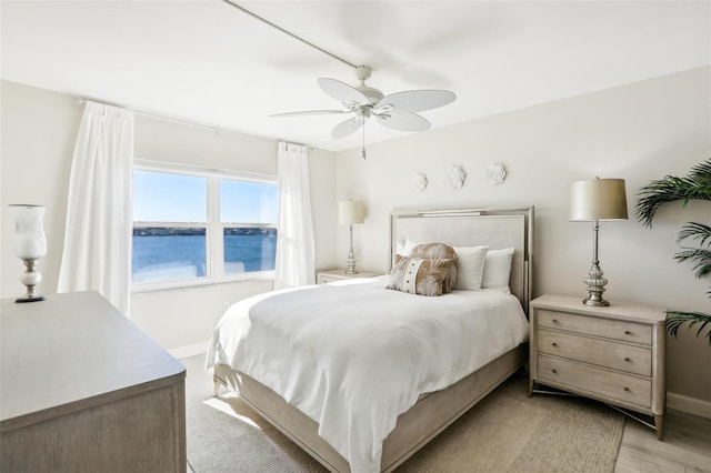 bedroom with light wood-type flooring, a water view, and ceiling fan