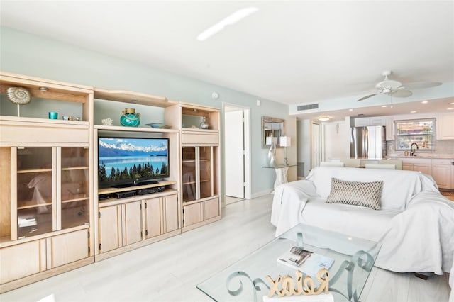 living room with light hardwood / wood-style flooring, ceiling fan, and sink