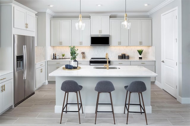 kitchen featuring decorative light fixtures, stainless steel appliances, a kitchen island with sink, and sink