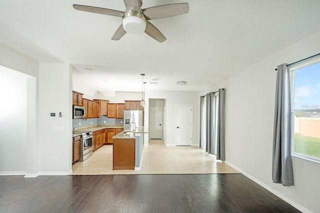 kitchen featuring ceiling fan, hanging light fixtures, light hardwood / wood-style flooring, a center island with sink, and appliances with stainless steel finishes