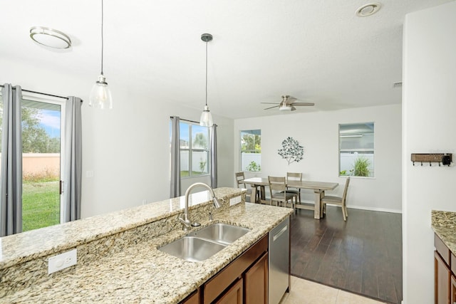 kitchen with decorative light fixtures, dishwasher, light stone counters, and sink