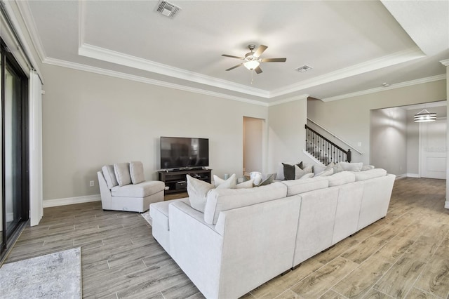 living room featuring ceiling fan, ornamental molding, a tray ceiling, and light hardwood / wood-style flooring