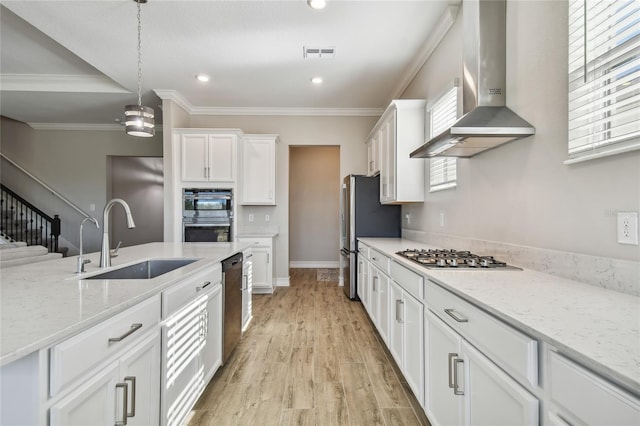 kitchen featuring hanging light fixtures, sink, wall chimney exhaust hood, appliances with stainless steel finishes, and white cabinetry