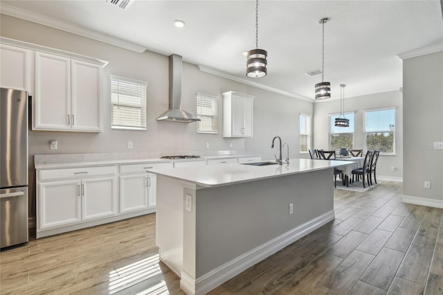 kitchen with white cabinetry, sink, wall chimney exhaust hood, stainless steel appliances, and an island with sink