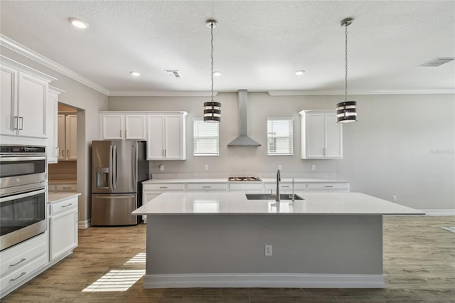 kitchen with a kitchen island with sink, wall chimney range hood, sink, white cabinetry, and stainless steel appliances