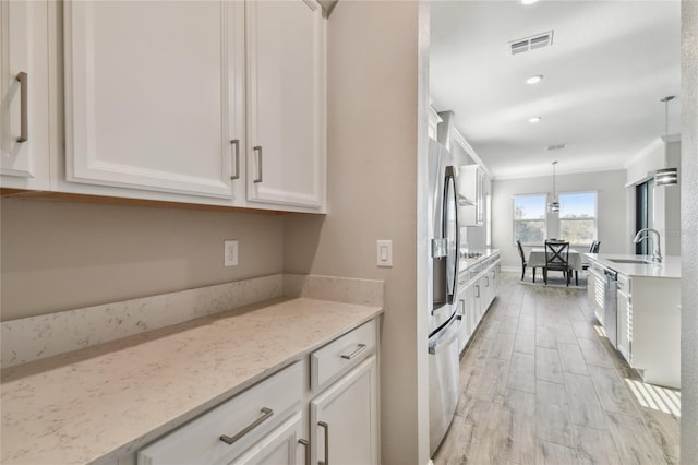 kitchen with light stone countertops, sink, decorative light fixtures, white cabinets, and appliances with stainless steel finishes