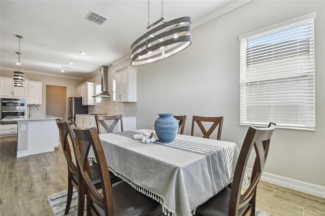 dining area with light hardwood / wood-style flooring, an inviting chandelier, ornamental molding, and sink