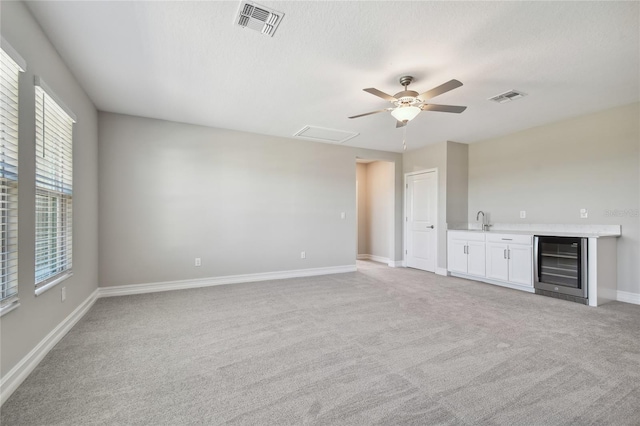 interior space featuring a healthy amount of sunlight, sink, light carpet, and wine cooler