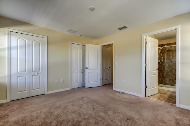 unfurnished bedroom with two closets, light colored carpet, and ensuite bath