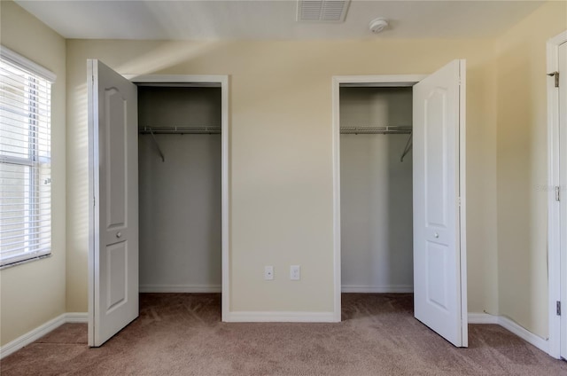 unfurnished bedroom featuring light carpet and multiple closets