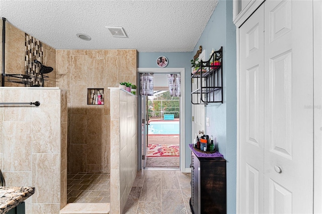 bathroom featuring vanity, a tile shower, a textured ceiling, and tile walls