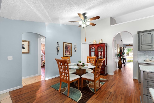 dining area with a textured ceiling, light wood-type flooring, vaulted ceiling, and ceiling fan