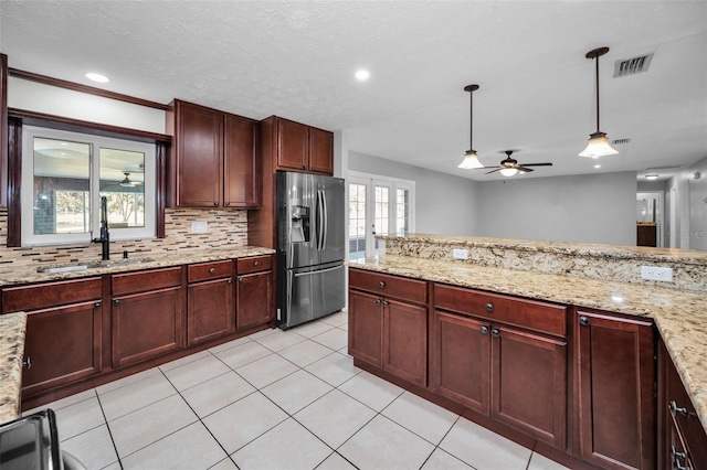 kitchen featuring sink, stainless steel fridge with ice dispenser, light stone counters, backsplash, and decorative light fixtures