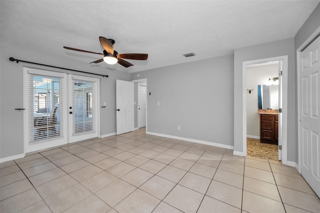 unfurnished bedroom with ensuite bath, ceiling fan, french doors, a textured ceiling, and light tile patterned flooring