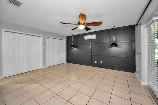 unfurnished bedroom featuring a textured ceiling, ceiling fan, multiple closets, and light tile patterned flooring