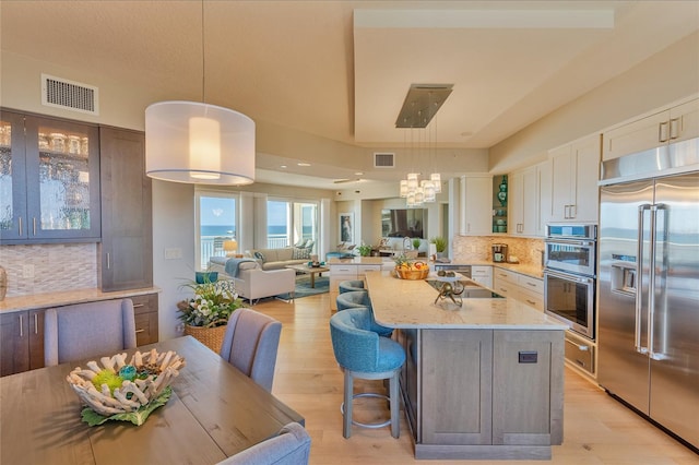 kitchen featuring appliances with stainless steel finishes, light wood-type flooring, decorative light fixtures, and white cabinetry