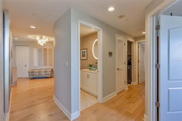 hallway with light wood-type flooring and a notable chandelier