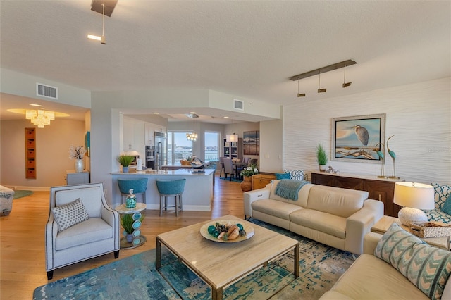 living room featuring a chandelier, a textured ceiling, and light hardwood / wood-style floors