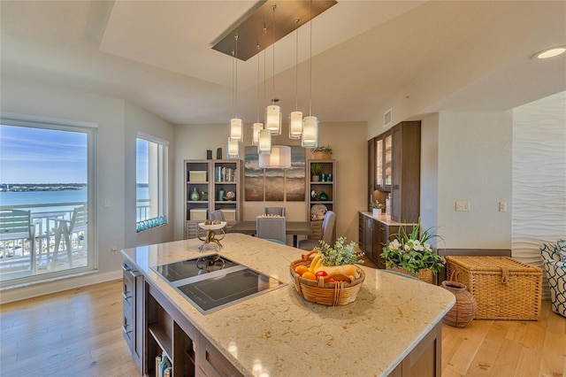 kitchen featuring a center island, black electric stovetop, a water view, light hardwood / wood-style flooring, and light stone countertops