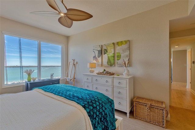 bedroom with ceiling fan, light hardwood / wood-style flooring, and a water view