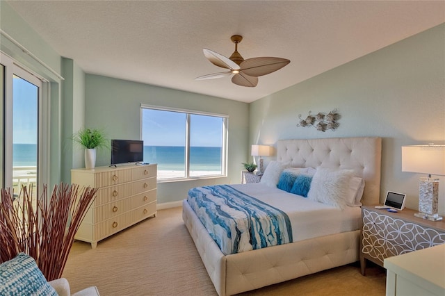 carpeted bedroom with ceiling fan, a water view, and a textured ceiling