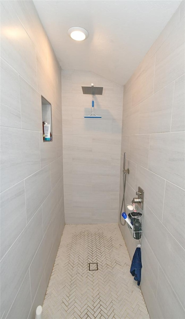 bathroom with a tile shower, vaulted ceiling, and tile walls