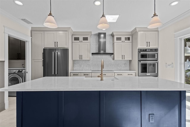 kitchen featuring washer / clothes dryer, appliances with stainless steel finishes, wall chimney range hood, and decorative light fixtures