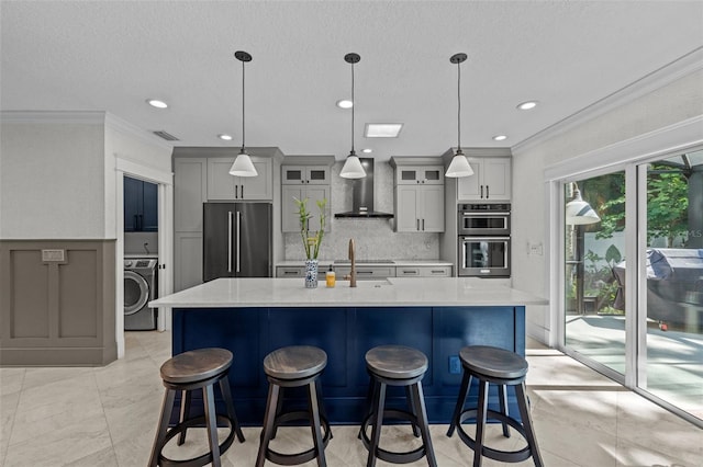 kitchen featuring gray cabinets, appliances with stainless steel finishes, wall chimney range hood, and washer / dryer