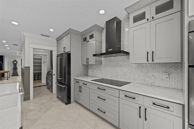 kitchen featuring light stone countertops, high end fridge, wall chimney range hood, and black electric cooktop