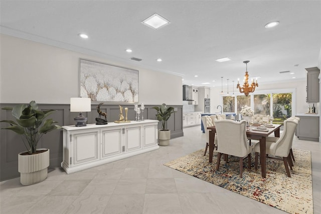 dining area featuring visible vents, wainscoting, ornamental molding, a chandelier, and a decorative wall