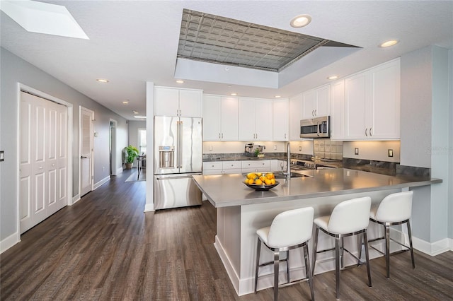 kitchen featuring white cabinetry, a raised ceiling, kitchen peninsula, a kitchen bar, and appliances with stainless steel finishes