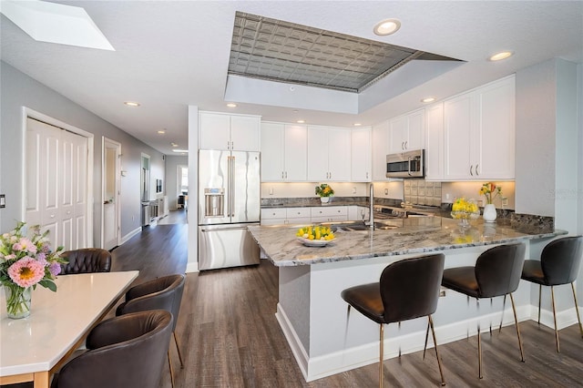 kitchen featuring kitchen peninsula, dark hardwood / wood-style floors, appliances with stainless steel finishes, a tray ceiling, and white cabinetry