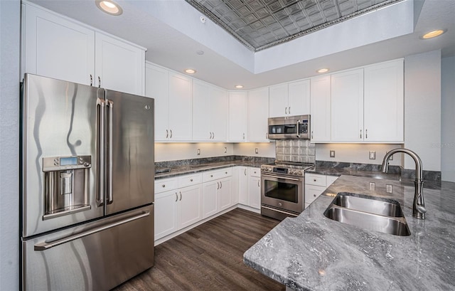 kitchen with appliances with stainless steel finishes, dark stone counters, dark wood-type flooring, sink, and white cabinetry