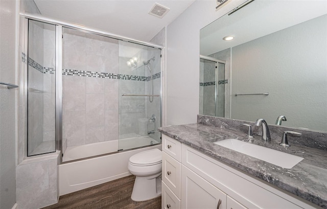 full bathroom with bath / shower combo with glass door, vanity, wood-type flooring, and toilet