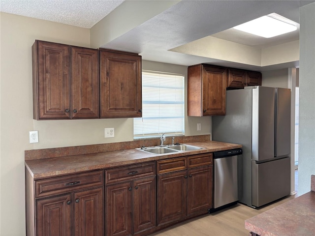 kitchen with sink, a textured ceiling, dark brown cabinets, light hardwood / wood-style floors, and stainless steel appliances