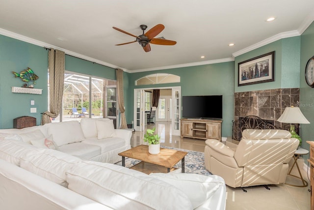 tiled living room featuring ceiling fan, crown molding, and a tiled fireplace