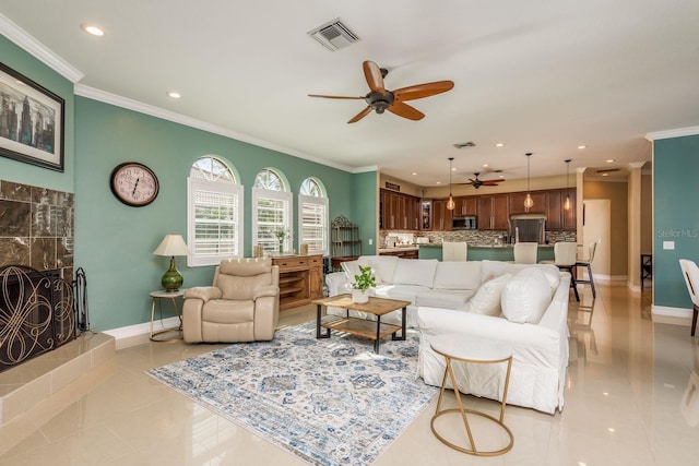 living room featuring a tile fireplace, light tile patterned floors, ceiling fan, and crown molding