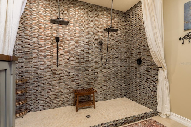 bathroom featuring tile patterned flooring, a tile shower, and baseboards