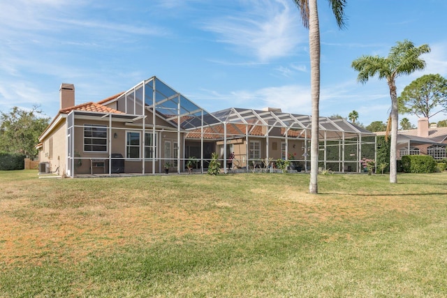 rear view of house featuring a lawn, a chimney, a lanai, central AC, and stucco siding